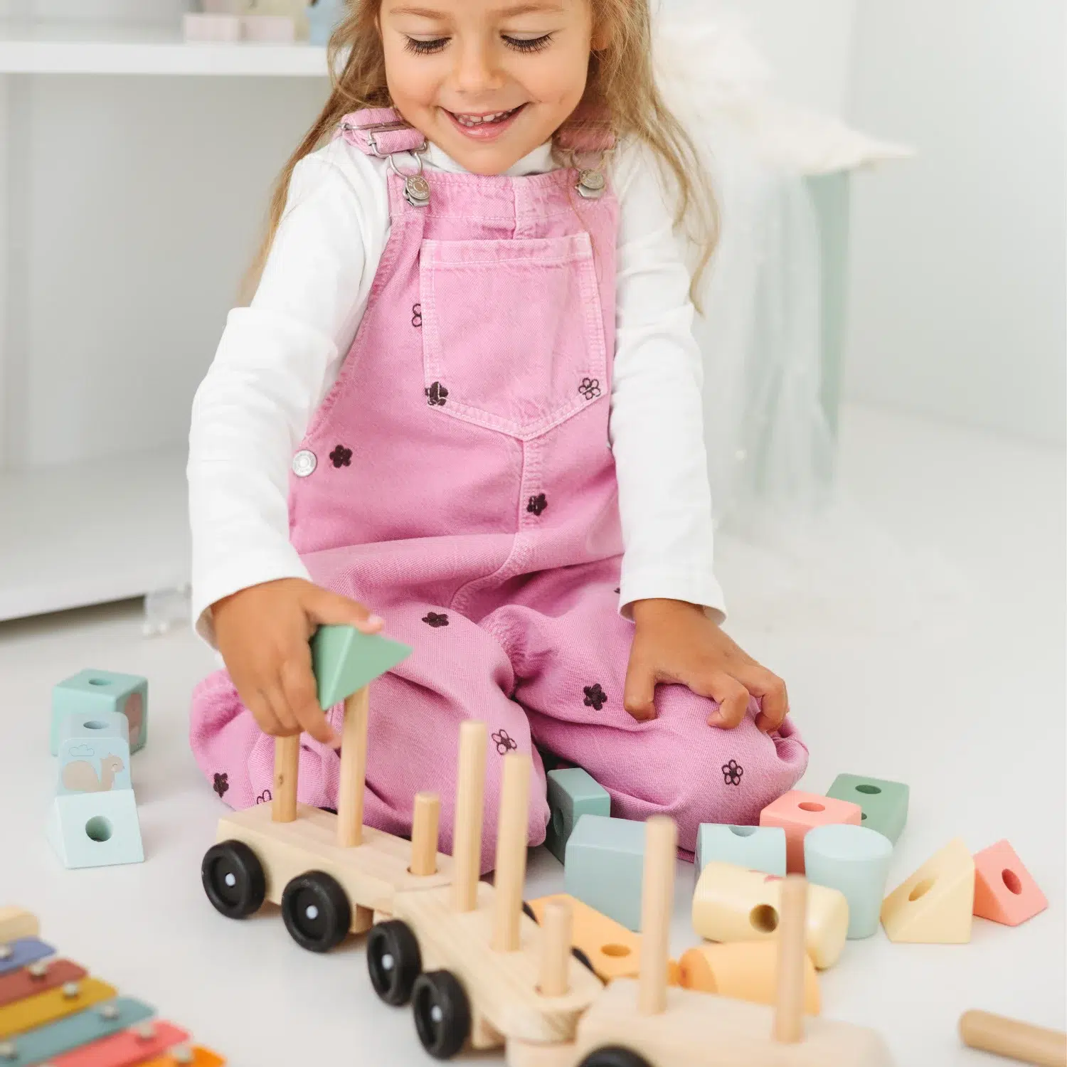 Lule drveni vozić – devojčica u igri Devojčica sedi na podu i slaže Lule drveni vozić za decu